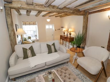 A living room with a sofa, armchair, side table, wooden beams, and a sideboard with lamps at Lower Pack Horse Cottage in Winchcombe