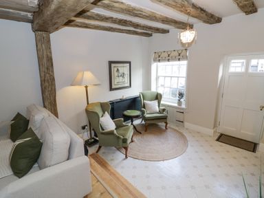 A sitting room with beige sofa green armchairs round rug and exposed wooden beams at Lower Pack Horse Cottage in Winchcombe