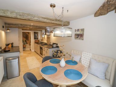 A kitchen with a round dining table set with blue placemats and a vase of flowers at Lower Pack Horse Cottage in Winchcombe