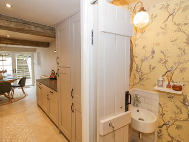 A kitchen area with beige cabinets and a small sink area with yellow floral wallpaper at Lower Pack Horse Cottage in Winchcombe