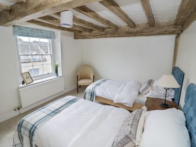 A bedroom with two single beds a chair by the window and a bedside table with a lamp at Lower Pack Horse Cottage in Winchcombe