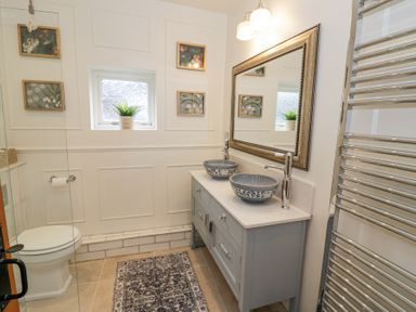 A bathroom with a toilet a double sink vanity a large mirror a window and floral wall art at Lower Pack Horse Cottage in Winchcombe