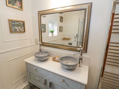 A bathroom with two round sinks on a vanity under a large framed mirror at Lower Pack Horse Cottage in Winchcombe