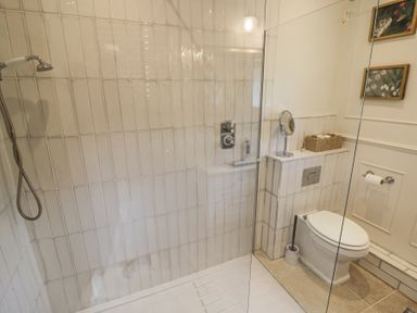 A bathroom with a walk-in shower and a toilet with a wicker basket on top at Lower Pack Horse Cottage in Winchcombe