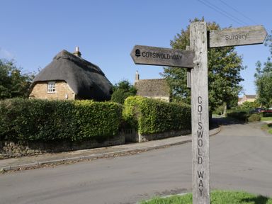 A rural road with a wooden signpost and a thatched roof house in Cotswold Way Winchcombe