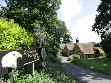 A sign for Cotswold Falconry Centre next to a road leading to stone buildings surrounded by trees at Lower Pack Horse Cottage in Winchcombe