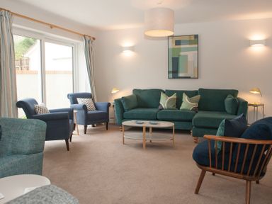 A living room with a green sofa blue armchairs wooden framed chair coffee table and wall art at Brooklands in Uplyme