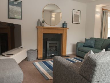 A living room with a grey sofa and teal sofa around a fireplace with a round mirror above at Brooklands in Uplyme