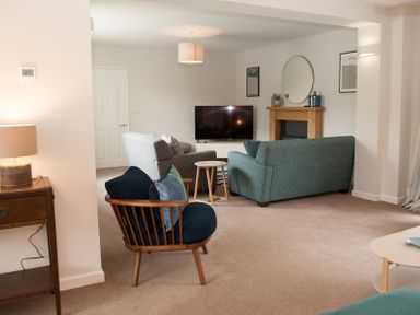 A living room with armchairs a sofa a television on a stand a wooden fireplace a round mirror and framed pictures at Brooklands in Uplyme