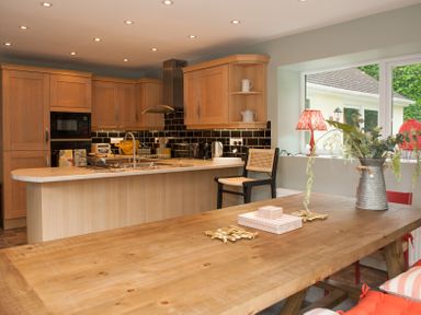 A kitchen with wooden cabinets dining table with flower vase and red lamps by window at Brooklands in Uplyme