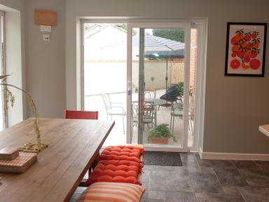 A dining area with a wooden table and red cushions by sliding glass doors leading to an outdoor patio at Brooklands in Uplyme