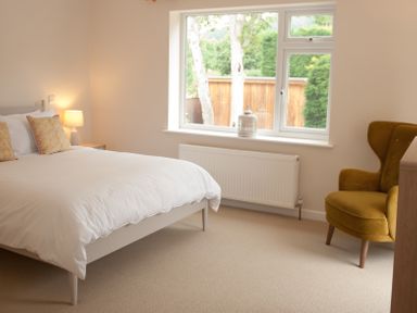 A bedroom with a bed a lamp on a bedside table a window and a mustard yellow armchair at Brooklands in Uplyme