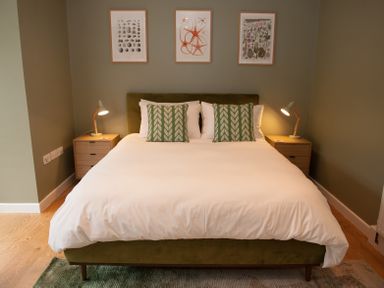 A bedroom with a bed a pair of bedside tables and lamps and three framed pictures on the wall at Brooklands in Uplyme