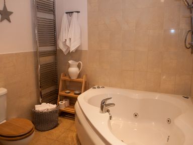 A bathroom with a corner bathtub wooden toilet seat wicker basket with towels and shelves with a white pitcher at Brooklands in Uplyme