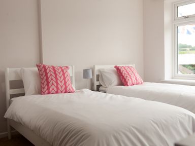 A bedroom with two single beds white bedding pink pillows and a window at Brooklands in Uplyme