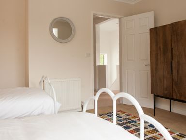 A bedroom with two beds a wooden wardrobe a round wall mirror and a multicolored rug at Brooklands in Uplyme