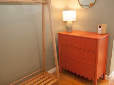 A wooden clothes rack next to a red three drawer dresser with a lamp and a speaker on top at Brooklands in Uplyme