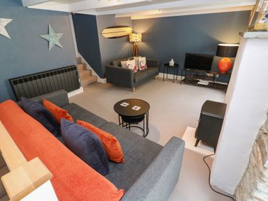 A living room with two sofas a television a lamp and stairs at Winterbrook Cottage in Mevagissey