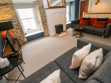 A living room with two gray sofas, a small black wood stove, two windows with stone surrounds and a TV on a stand at Winterbrook Cottage Mevagissey