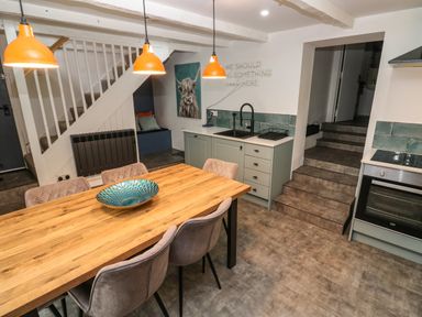 A kitchen and dining area with a wooden table, six chairs, orange pendant lights, stairs, and a sink at Winterbrook Cottage in Mevagissey