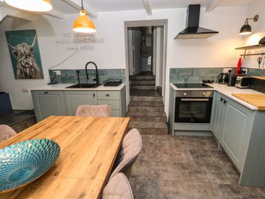 A kitchen with wooden dining table blue green cabinets black sink and oven and stairs leading to a hallway at Winterbrook Cottage in Mevagissey