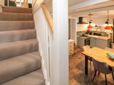 Carpeted stairs next to a kitchen with wooden dining table and chairs at Winterbrook Cottage in Mevagissey
