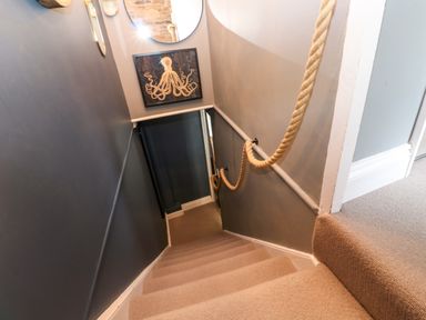A carpeted staircase with rope handrail and octopus artwork on wall at Winterbrook Cottage in Mevagissey