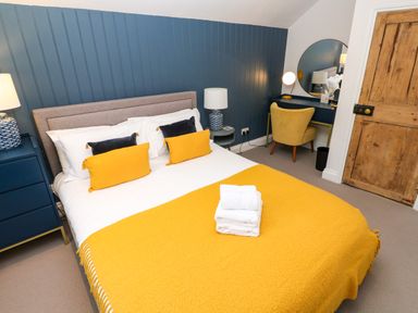 A bedroom with a bed with yellow and black pillows a yellow blanket bedside tables lamps a wooden door and a desk with a yellow chair at Winterbrook Cottage Mevagissey