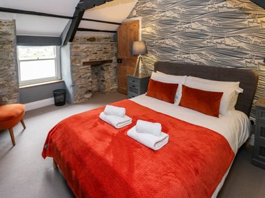 A bedroom with stone walls orange bedspread and pillows bedside tables and lamp at Winterbrook Cottage in Mevagissey