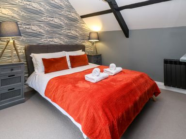 A bedroom with a double bed with orange bedding and two bedside tables with lamps at Winterbrook Cottage in Mevagissey
