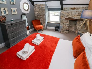 A bedroom with a bed with orange pillows and blanket a dresser chair stone wall and window at Winterbrook Cottage in Mevagissey