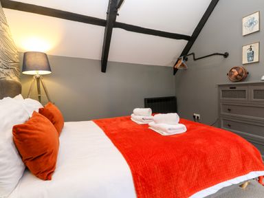 A bedroom with a bed covered with a red blanket and orange pillows a lamp dresser and hanging rail at Winterbrook Cottage in Mevagissey