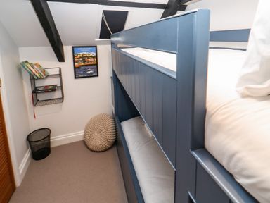 A bedroom with blue bunk beds a round knitted cushion a wire wall shelf with books and a framed picture on the wall at Winterbrook Cottage in Mevagissey