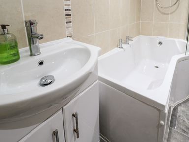 A bathroom with a white sink and a bathtub with taps at Winterbrook Cottage in Mevagissey