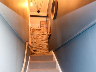 A carpeted staircase with rope handrail stone wall and two round mirrors on blue walls at Winterbrook Cottage in Mevagissey