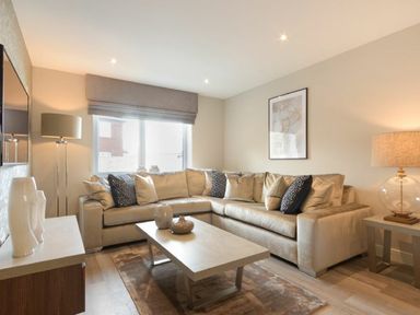 A living room with a beige sectional sofa a coffee table with decorative vases a floor lamp and a table lamp at Sans Souci in Seahouses