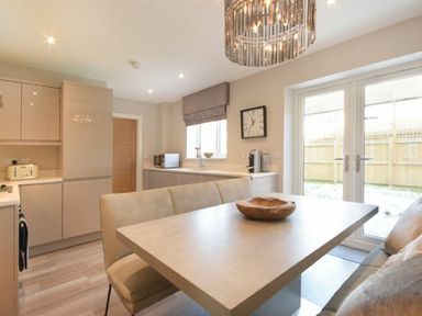 A kitchen with a dining table and bench seating a clock on the wall and glass doors leading outside at Sans Souci in Seahouses