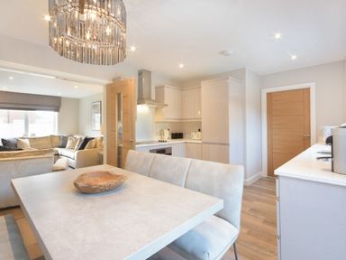 A kitchen and dining area with a table and cushioned bench and a living room with sofas at Sans Souci in Seahouses