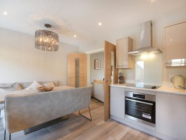 A kitchen area with an oven stove and kettle next to a seating area with a sofa and dining bench at Sans Souci in Seahouses
