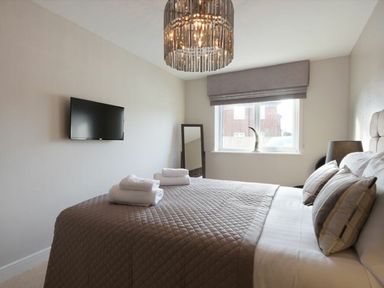 A bedroom with a bed covered in a quilt and towels on it a wall-mounted TV a window with a blind and a standing mirror at Sans Souci in Seahouses
