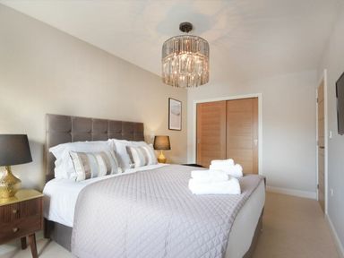 A bedroom with a double bed a gray headboard bedside tables with lamps folded towels on the bed and wooden closet doors at Sans Souci in Seahouses