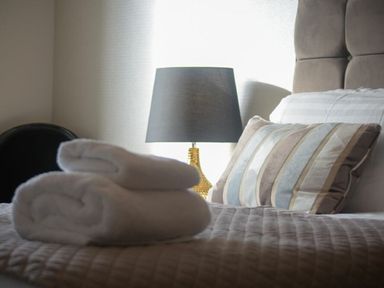 A bed with folded towels a striped pillow and a bedside lamp at Sans Souci in Seahouses