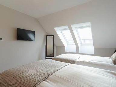 A bedroom with two beds a wall-mounted tv and two skylight windows at Sans Souci in Seahouses