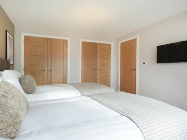 A bedroom with two twin beds white bedding wooden doors and a wall mounted tv at Sans Souci in Seahouses