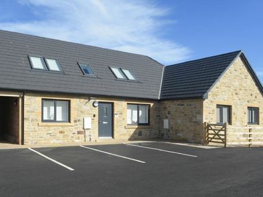 Stone building with black roof and multiple windows and parking spaces in front at Sans Souci in Seahouses