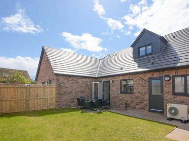 A backyard with green grass table and chairs fenced yard and a brick house with windows and door at Sans Souci in Seahouses