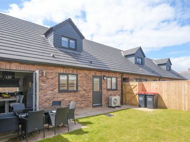 A backyard with outdoor dining table and chairs next to a brick house with black windows and doors at Sans Souci in Seahouses