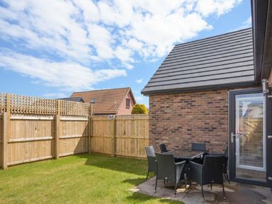 A small fenced backyard with a patio table and chairs beside a brick building at Sans Souci in Seahouses