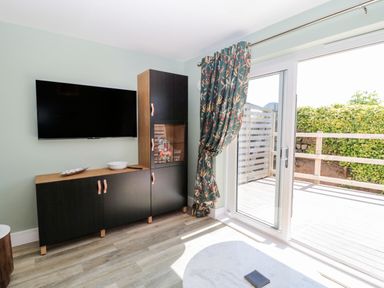 A living area with a wall-mounted TV and black cabinets next to sliding glass doors with floral curtains at Rose Lodge in High Newton-by-the-Sea near Embleton
