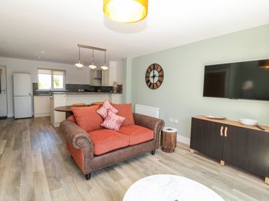 A living room with an orange and brown sofa a wall clock and a flat screen tv at Rose Lodge in High Newton-by-the-Sea near Embleton